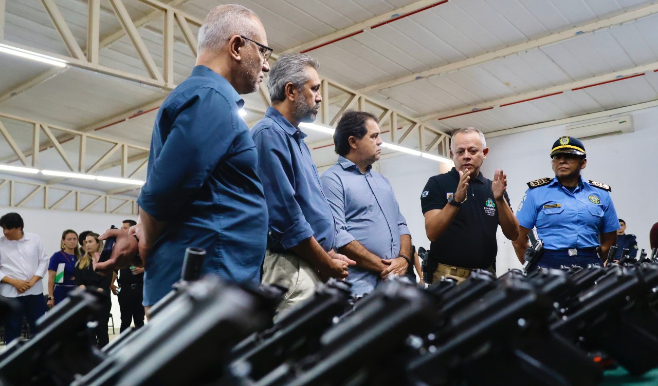 prefeito evandro, governador elmano e integrantes da guarda municipal conversam em frente à mesa onde estão dispostas as armas doadas